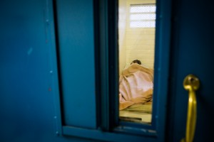 An inmate is visible through the cell door with window