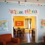 Inside Edgewood, a double doorway way leading to a common room with chairs and tables. Artwork and maps hang around door way.