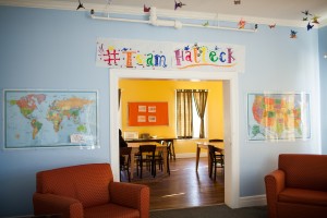 Inside Edgewood, a double doorway way leading to a common room with chairs and tables. Artwork and maps hang around door way.