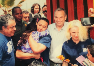 Left to Right: Enrique Morones, A Customs and Border Patrol officer, father and daughter hugging, Mayor Falconer, and a Border Angel. The first hug at Door of Hope after the construction of the fence. Hung on the wall of Enrique Morones’ office at the Sherman Heights Community Center.