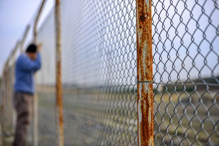Wire fence in front sad poor man standing