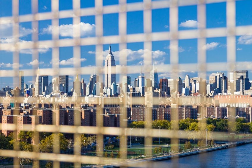 New York City downtown skyline skyscrapers view seen through the bars of a fence on the williamsburg bridge