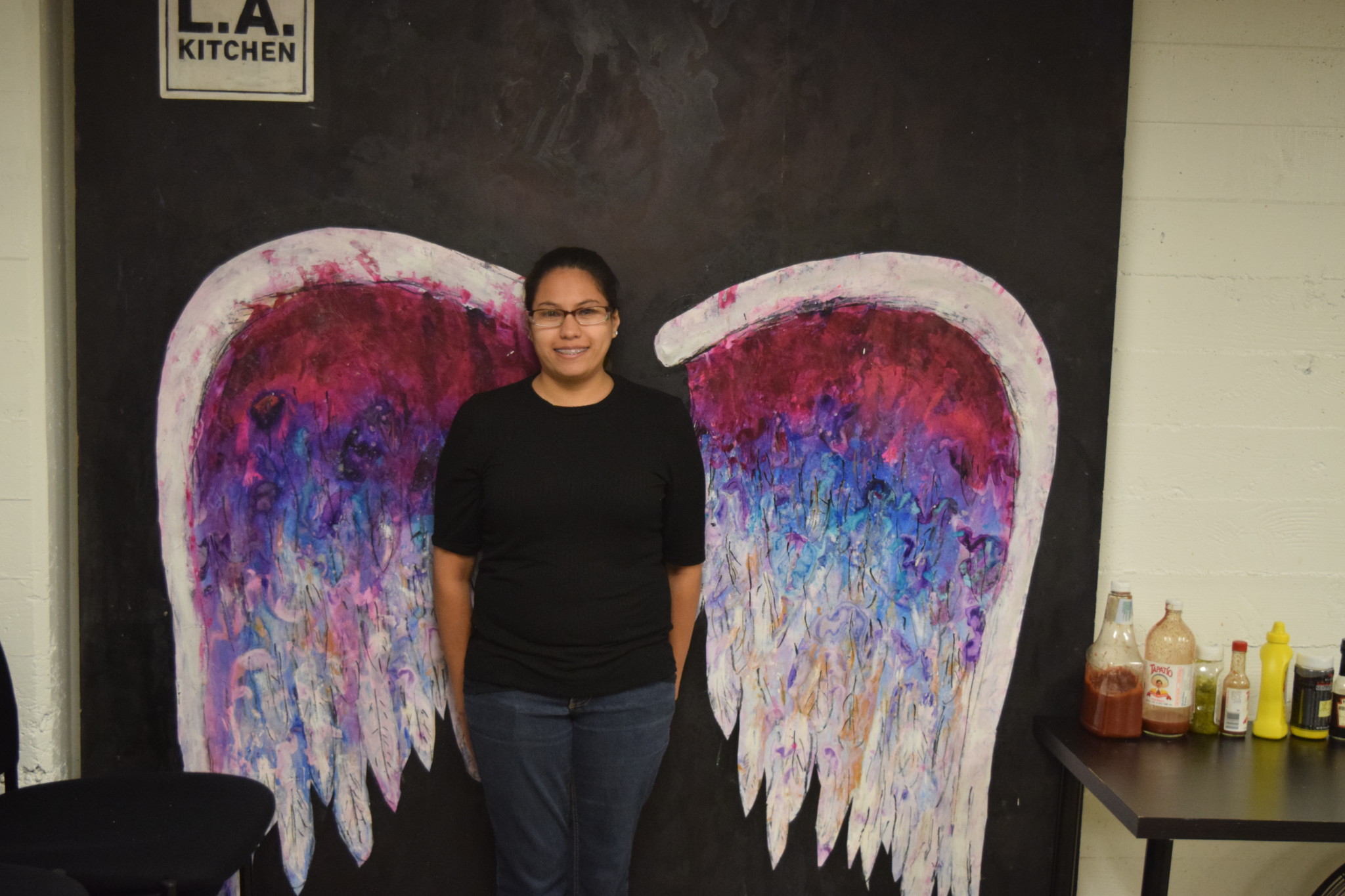 Sandra Vasquez posing in front of the angel wings painted onto a wall at L.A. Kitchen