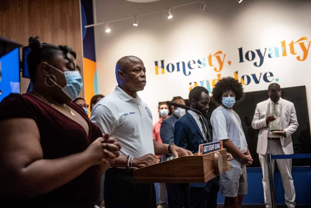 New York City Mayor Eric Adams, pictured in a white shirt, in a press conference about addressing youth homelessness with a plan led by youth with experience.