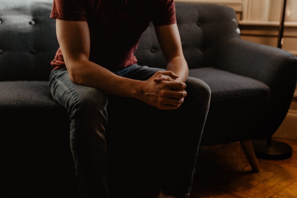 Image of a non-identifiable young person in jeans and a t-shirt on a couch with his hands folded for story "New York City Community Teams Aim to Meet Psychiatric Needs of Low-Income Youth"