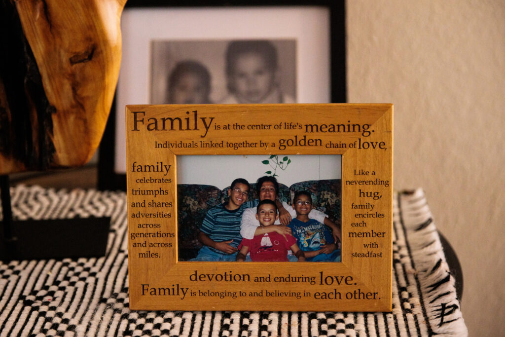 An old picture of three boys and their mother smiling sits inside a frame with words about family and love.