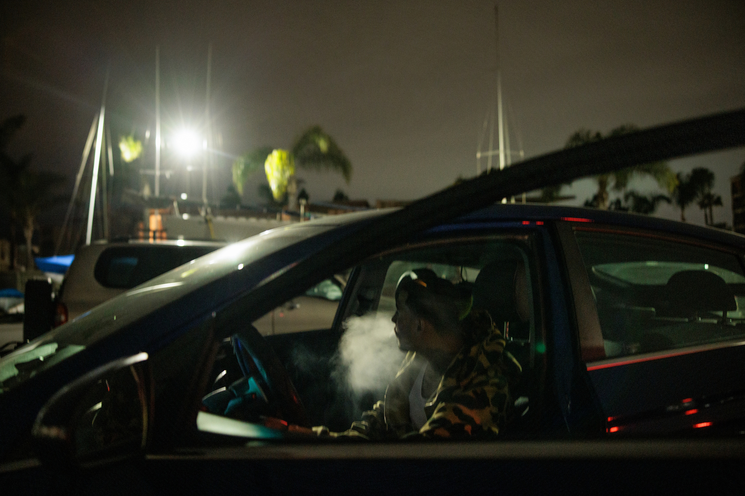 A man smokes in his car at night outside a yacht club.