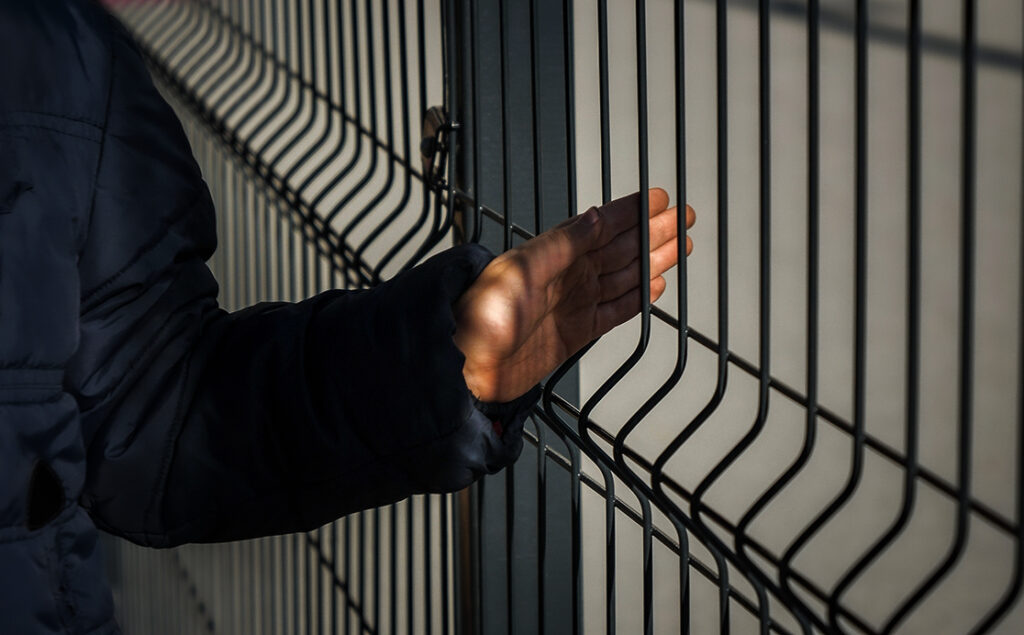Closeup of little child hand holding net metal fence.